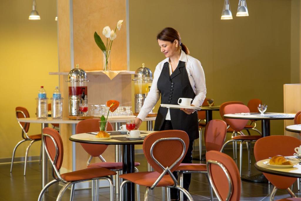 a woman holding a cup of coffee at a table in a restaurant at Hotel Mediterraneo in Livorno
