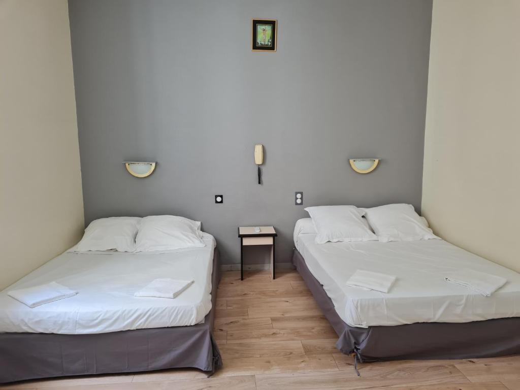 twee bedden in een kleine kamer met een tafel bij Hôtel Le Milan in Lourdes