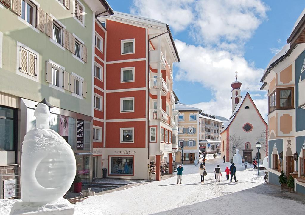 Un groupe de personnes marchant dans une rue avec des bâtiments dans l'établissement Hotel Maria, à Ortisei