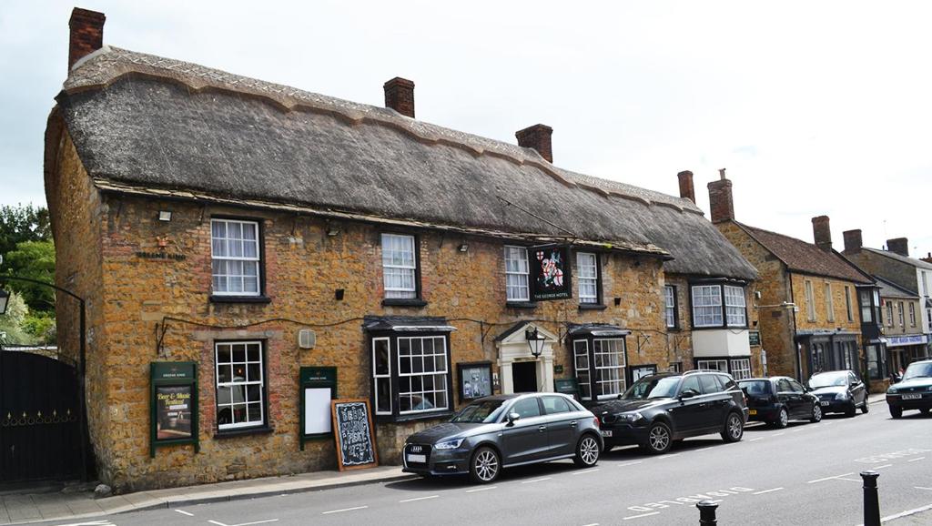 an old brick building with cars parked in front of it at The George Hotel in Castle Cary