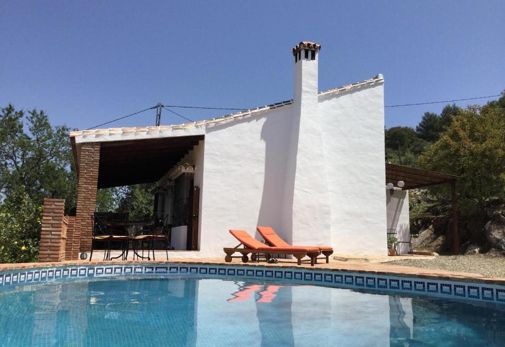 una casa con piscina y 2 sillas junto a ella en Sunny hillside casita in Guaro, en Guaro