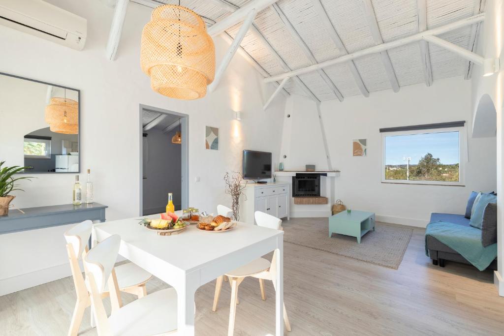 comedor blanco y sala de estar con mesa y sillas blancas en Palmeiras Cottages en Mexilhoeira Grande