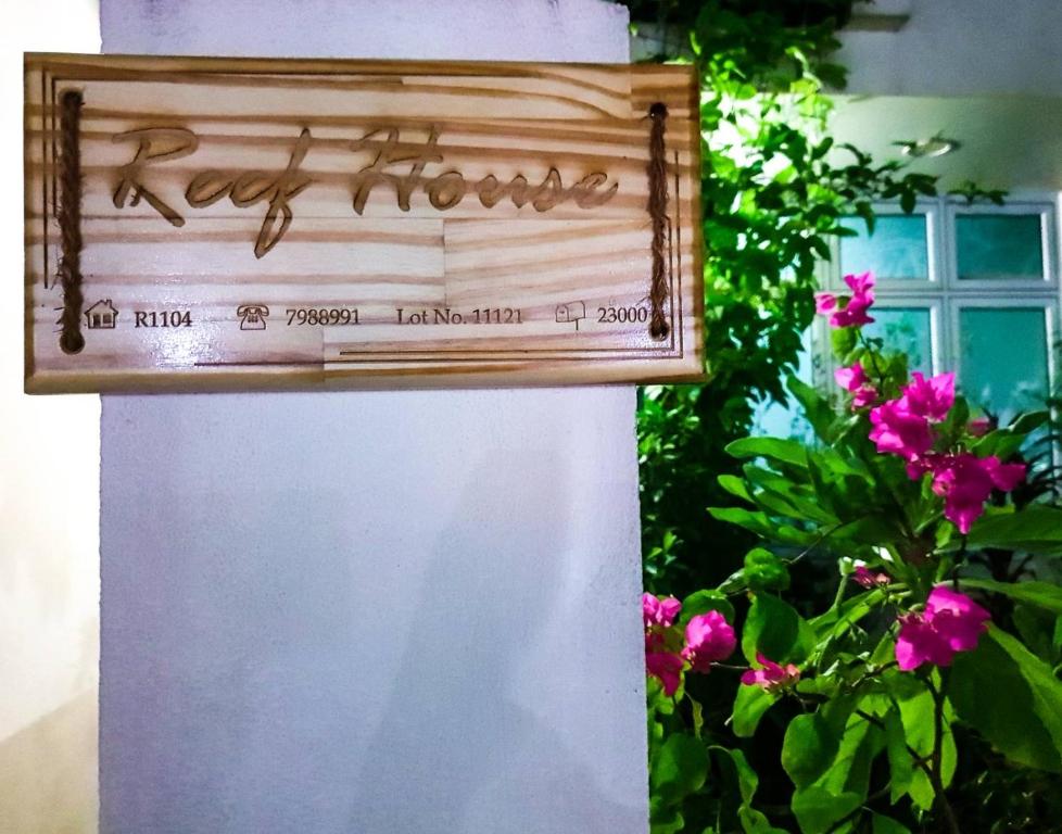 Reef Guest House في مدينة ماليه: علامة تقرأ في المنزل على عمود مع الزهور