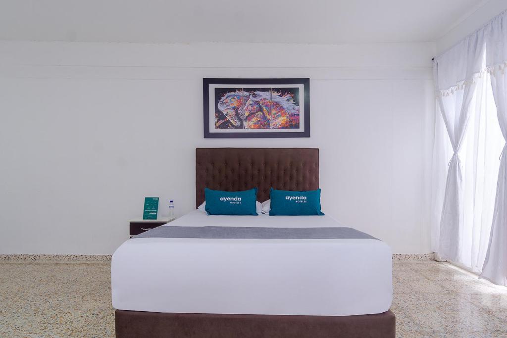 1 dormitorio con 1 cama blanca grande con almohadas azules en Ayenda Hotel Paraiso Chipichape, en Cali