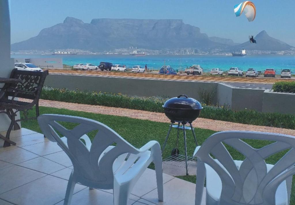 a grill and chairs on a patio with a view of the ocean at Sea Spray in Bloubergstrand