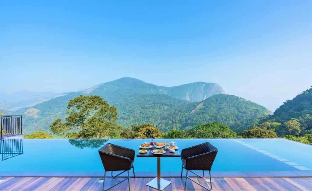 a table and chairs on a deck with a view of mountains at Shola Crown Resort - Munnar in Chinnakanal