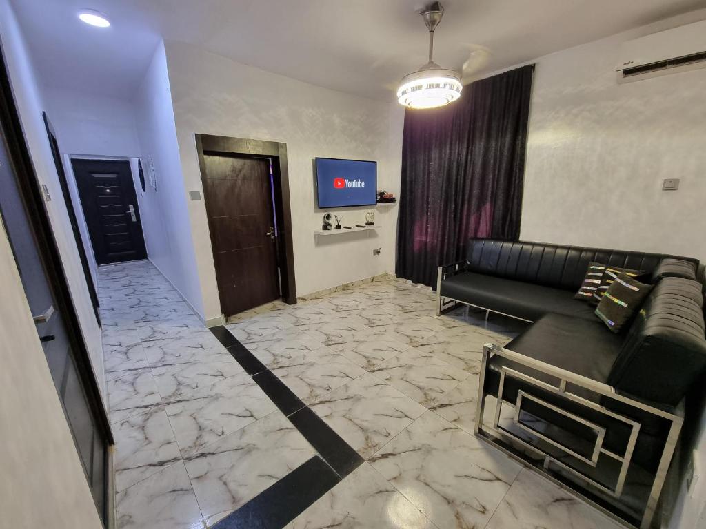 uma sala de estar com um sofá preto e uma televisão em CG Apartments em Ikeja