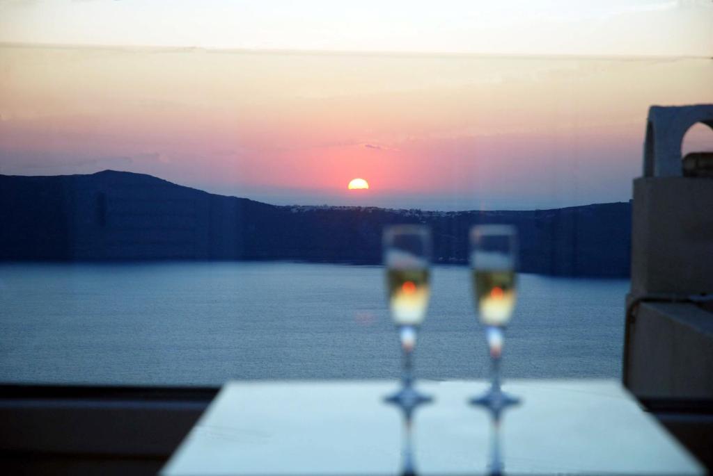 two glasses of wine sitting on a table with the sunset at Reverie Santorini Hotel in Firostefani