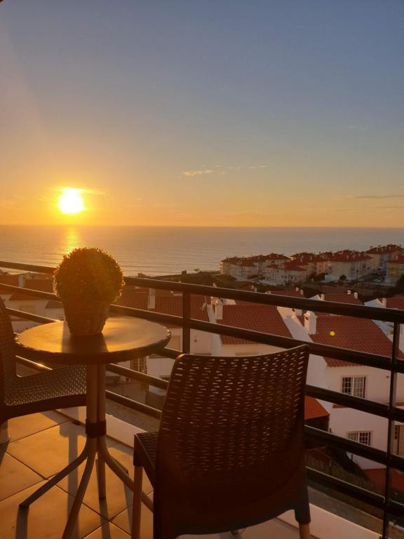 einen Tisch und Stühle auf einem Balkon mit Blick auf den Sonnenuntergang in der Unterkunft RIBEIRA D'ILHAS CENTRAL HOME in Ericeira