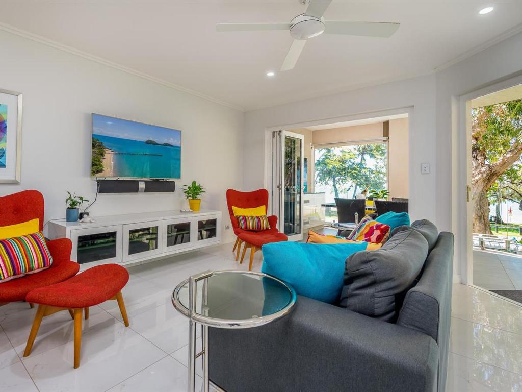 uma sala de estar com um sofá cinzento e cadeiras vermelhas em Coral Horizons by Elysium Collection em Palm Cove
