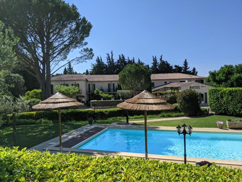 a swimming pool with umbrellas in front of a house at Hôtel Le Pradet in Vacqueyras