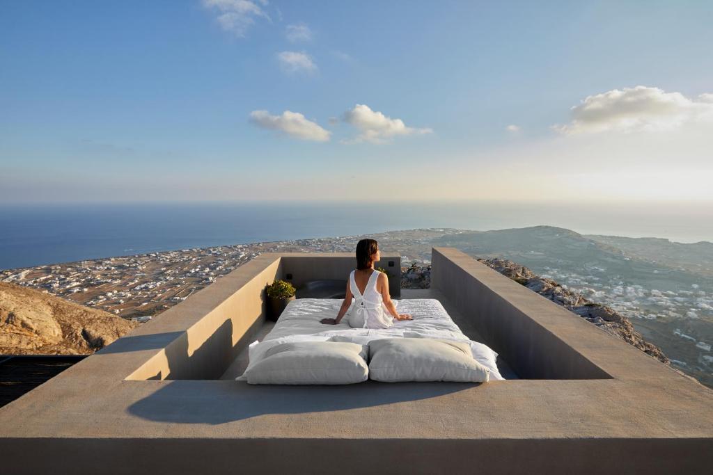 una mujer sentada en una cama en la cima de una montaña en Santorini Sky, The Lodge, en Pirgos