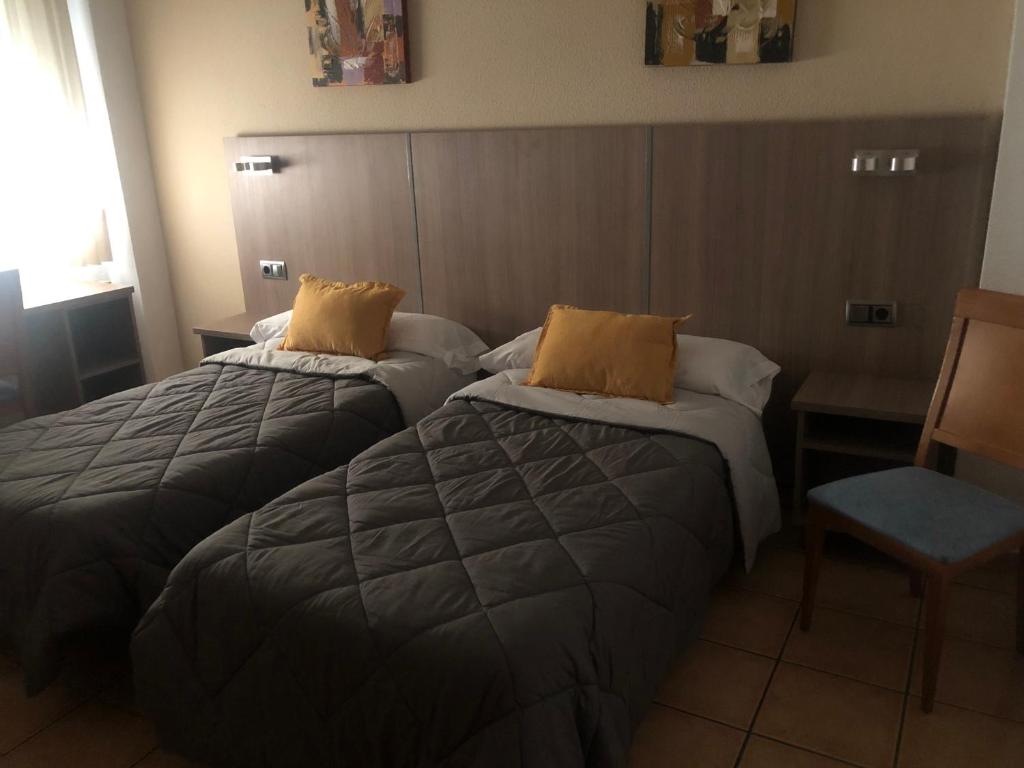 a hotel room with two beds and a chair at Hostal De La Rosa in Valdemoro