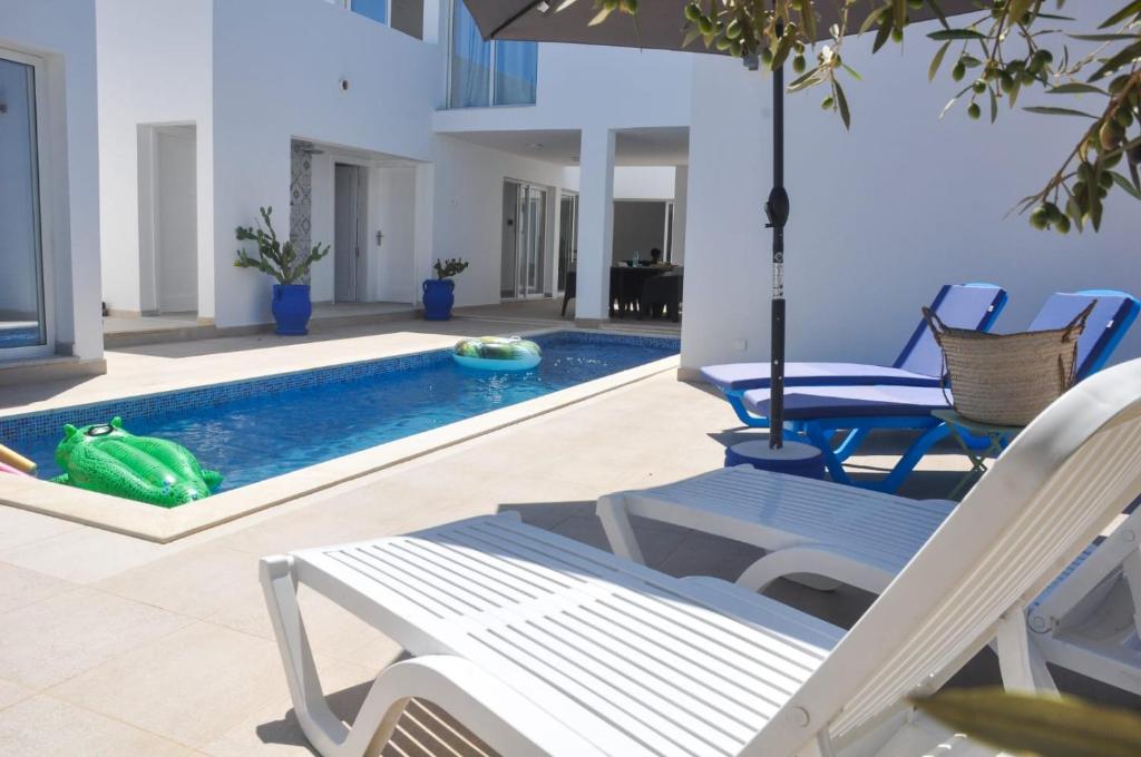 uma piscina com cadeiras e um guarda-sol e um sapo verde na água em Villa Salem Maison d'architecte toute équipée & piscine em Arkou