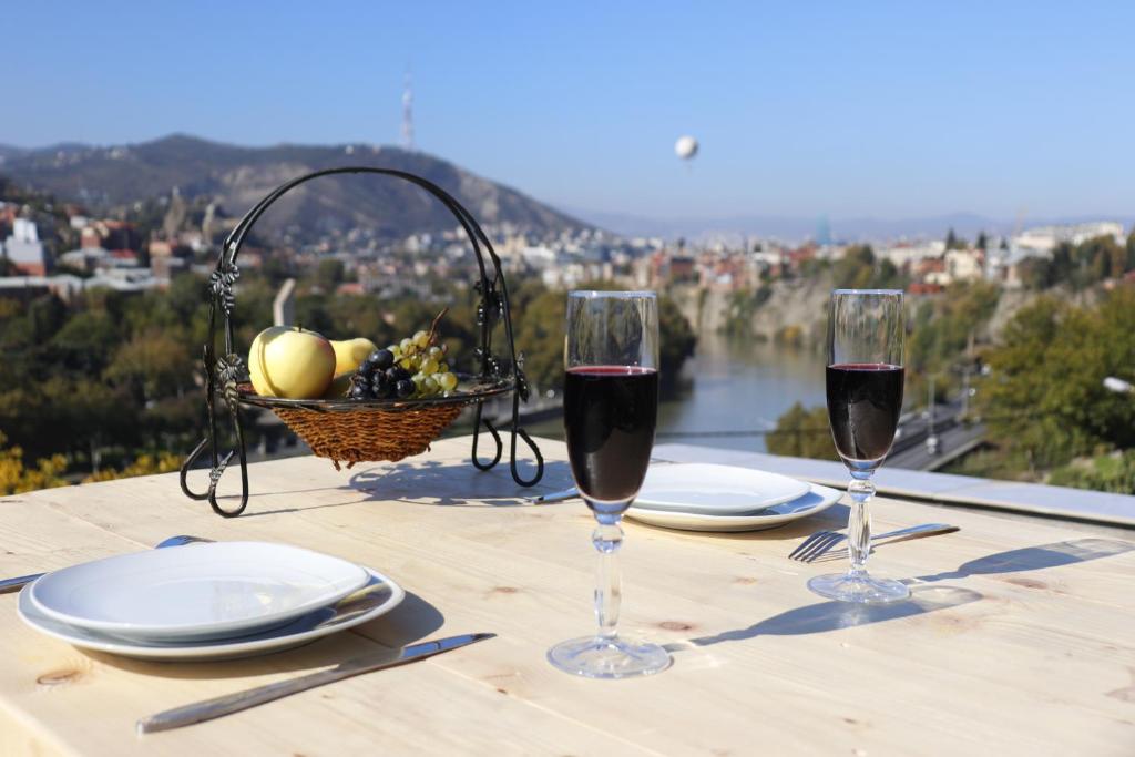 two glasses of wine on a table with a basket of fruit at Hotel Tradicia in Tbilisi City