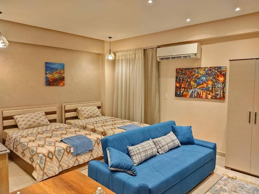 a bedroom with two beds and a blue couch at Eco Inn - Sherook993g2 Studio in Madīnat ash Shurūq