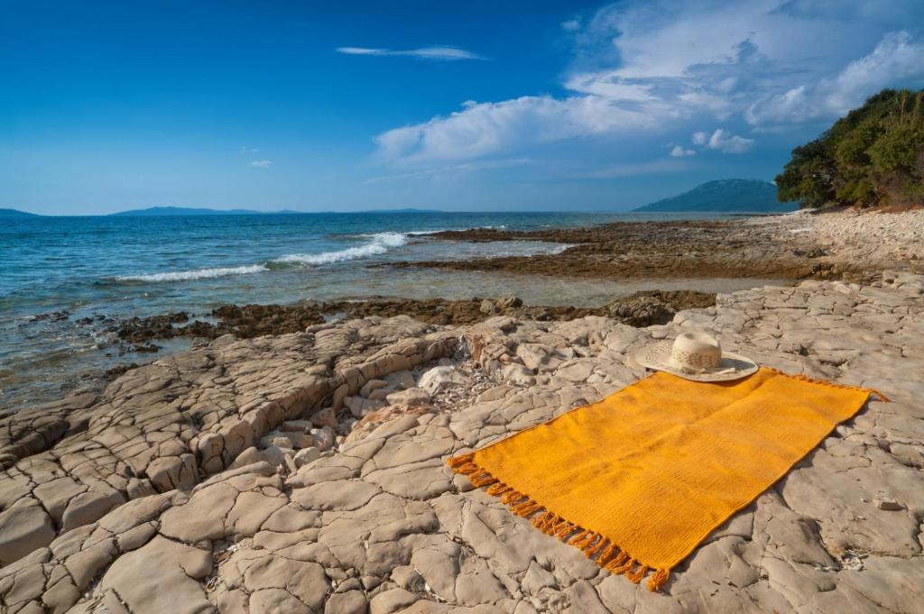 a yellow towel on a rocky beach next to the ocean at Studio 4827-3 for 4 Pers in Nerezine in Nerezine