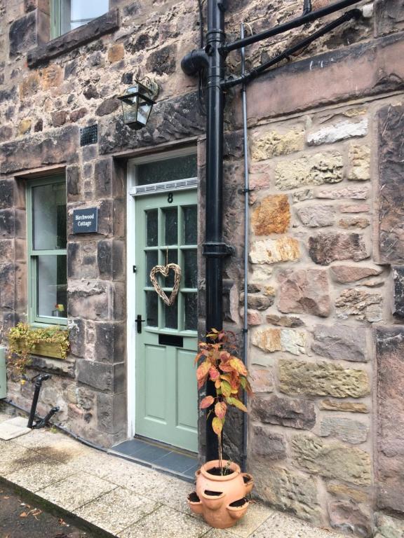 a stone building with a green door and a potted plant at Birchwood Cottage - In the Heart of Wooler in Wooler
