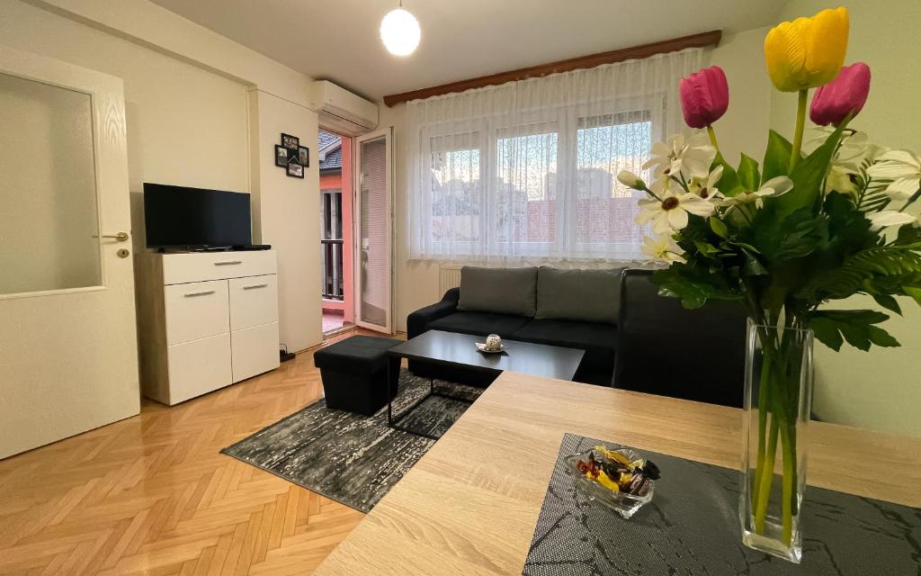 a living room with a black couch and flowers in a vase at Apartman Central in Bijeljina