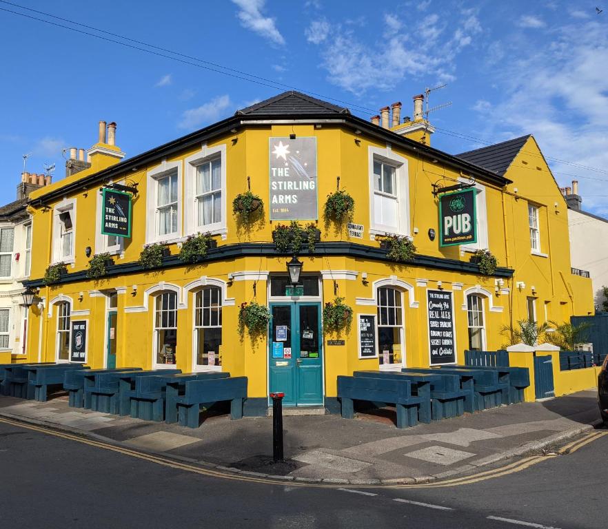 a yellow building with blue benches in front of it at The Stirling Arms Pub & Rooms in Brighton & Hove