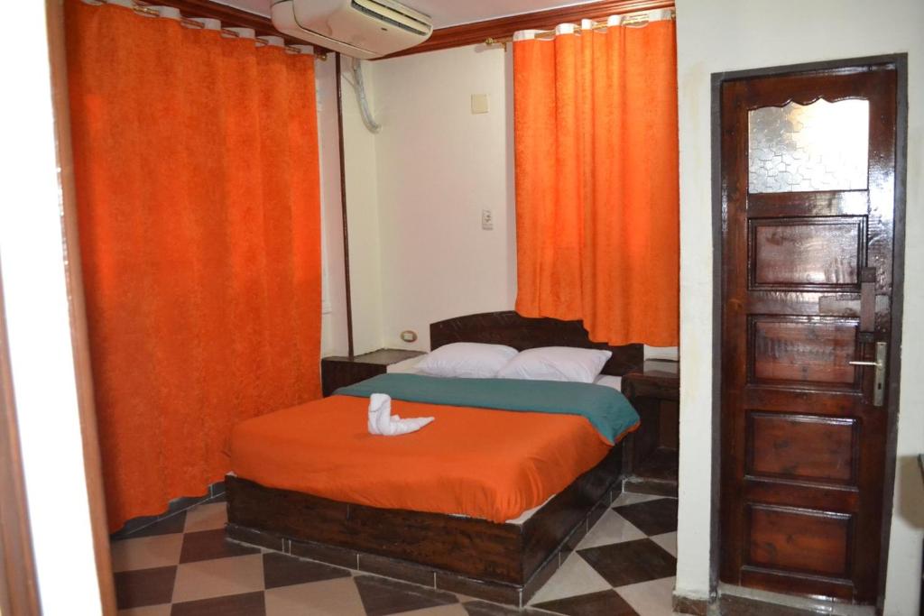 um quarto com uma cama com cortinas cor de laranja e uma porta em Kulih Nubian House em Shellal
