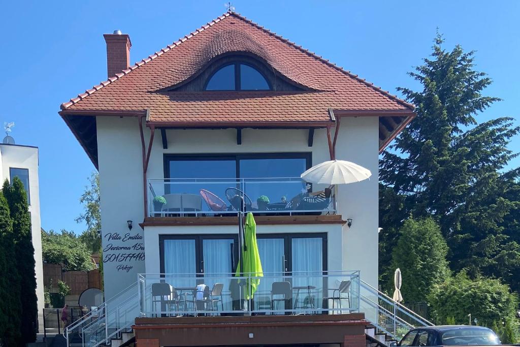 a house with a balcony with chairs and an umbrella at Pokoje Villa Emilia in Charzykowy