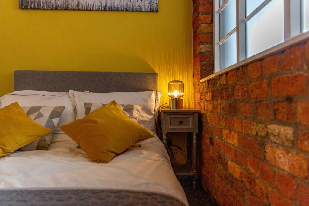 a bed with yellow pillows next to a brick wall at Lovely Central 1 Bed Apartment Sleeps 4 in Sheffield