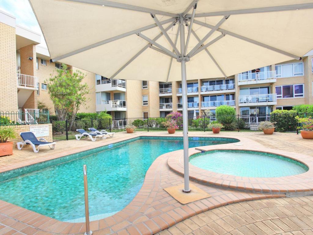 a pool with an umbrella next to a building at Headlands 10 Two Bedroom Beachside Apartment with Magical Ocean Views Great Value for Money in Alexandra Headland