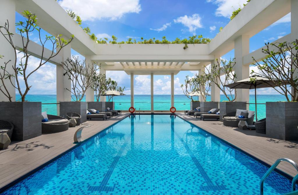 a swimming pool with chairs and the ocean in the background at Paris Deli Danang Beach Hotel in Da Nang