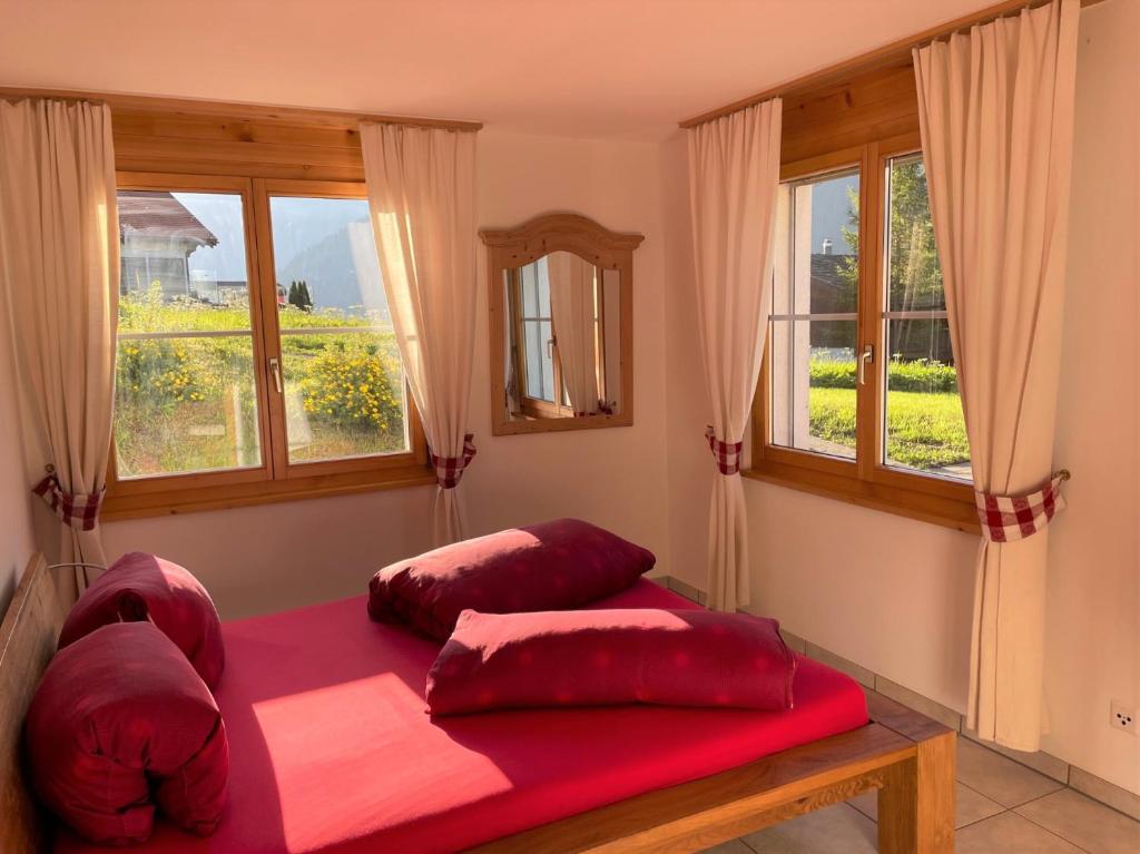 a bedroom with two red pillows on a bed with windows at Ferienwohnung CASA URSIN Val Lumnezia in Lumbrein