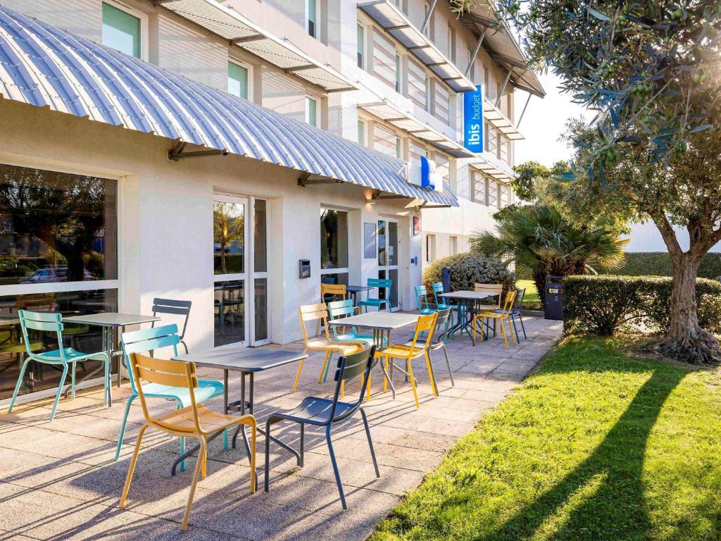 un patio avec des tables et des chaises en face d'un bâtiment dans l'établissement ibis budget Carcassonne Aéroport - A61, à Carcassonne