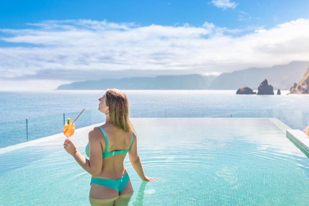 a woman in a bikini holding a drink in a swimming pool at Aqua Natura Bay in Porto Moniz