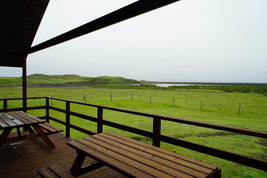una terraza de madera con un banco y vistas a un campo en Riverside Lodge with breathtaking view, en Kirkjubæjarklaustur