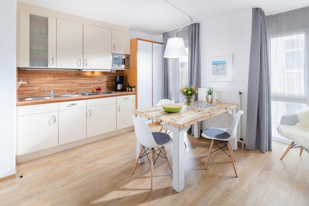 ノルダーナイにあるFerienwohnung Kleine Luiseの白いキャビネット、木製テーブルと椅子付きのキッチンが備わります。
