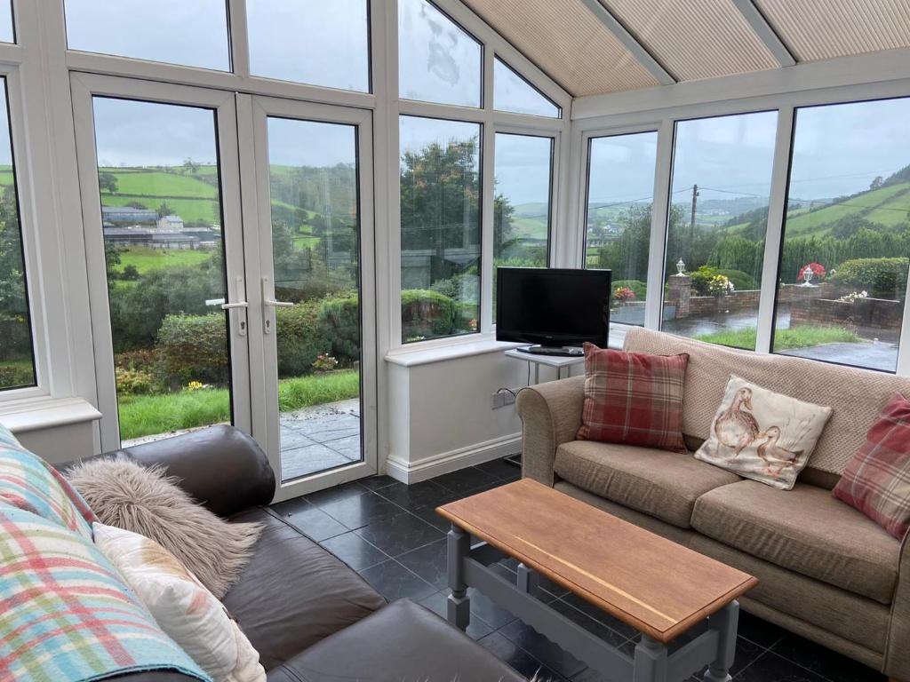 a living room with a couch and a tv and windows at 4 bedroom bungalow in peaceful countryside with log burner - Talar Deg, Capel Madog in Bow Street