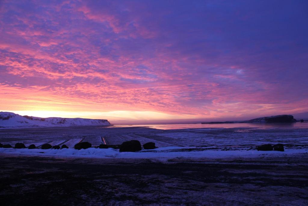 a sunset over a field with snow on the ground at Hótel Dyrhólaey in Vík
