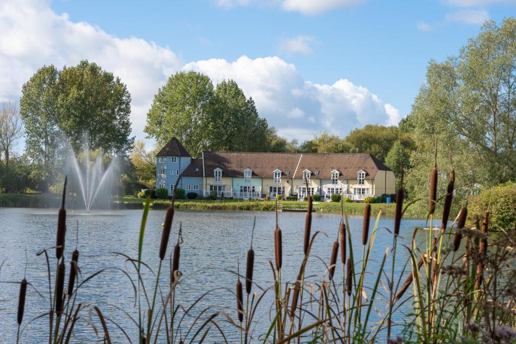 a large house sitting on the edge of a lake at Mayfly Lodge in South Cerney