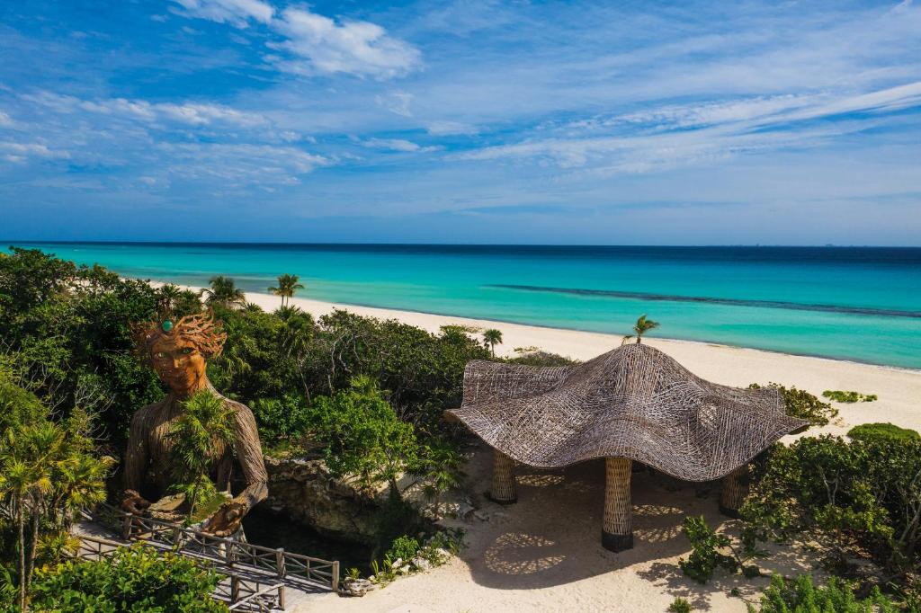 eine Statue und einen Sonnenschirm am Strand in der Unterkunft Palmaïa The House of AïA All Inclusive Wellness Resort in Playa del Carmen