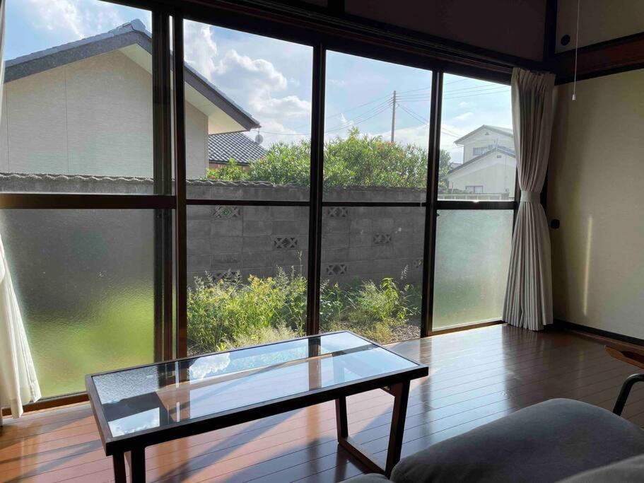 昭和の家ume في فوكوشيما: غرفة معيشة مع طاولة زجاجية ونوافذ كبيرة