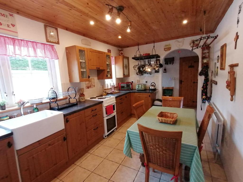 uma cozinha com armários de madeira, uma mesa e um lavatório em Carnowen Cottage em Ringsend