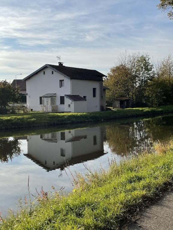 une maison blanche à côté d'une nappe d'eau dans l'établissement Maison de campagne proche Lac de Bouzey, à Chaumousey