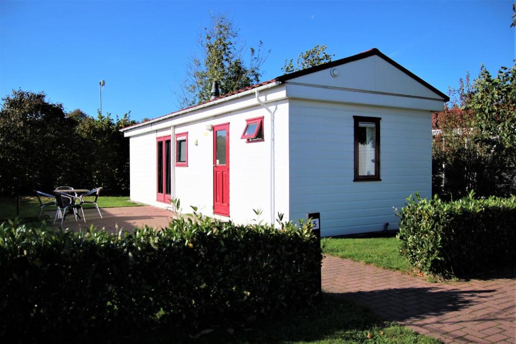ein kleines weißes Gebäude mit roten Türen und einem Tisch in der Unterkunft Hofgalow Chalet op camping "De Stal" in Drijber