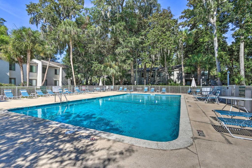 een zwembad met blauwe stoelen en bomen bij Hilton Head Tropical Condo Walk to Coligny Beach! in Hilton Head Island