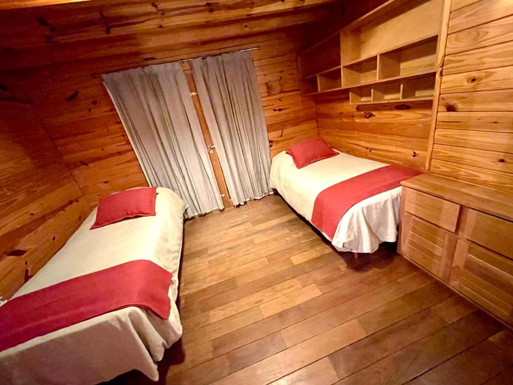 two beds in a room with wooden walls and wood floors at Apart Quillen 1 in San Martín de los Andes