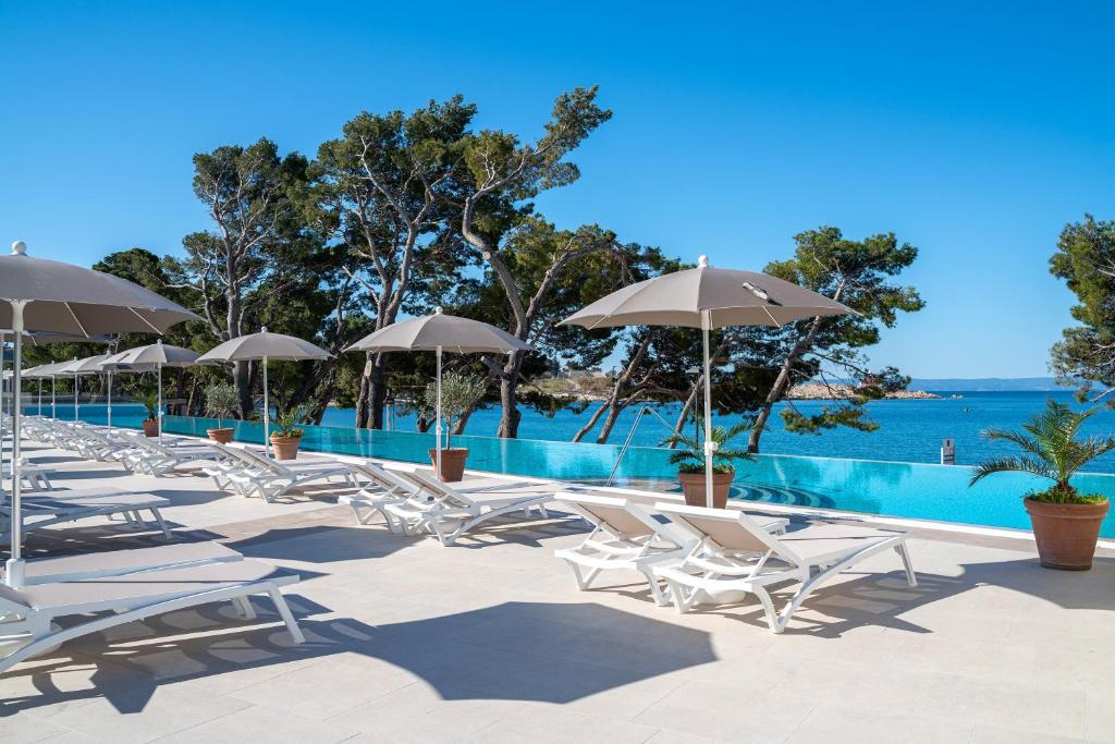 uma fila de cadeiras e guarda-sóis ao lado de uma piscina em Valamar Meteor Hotel em Makarska
