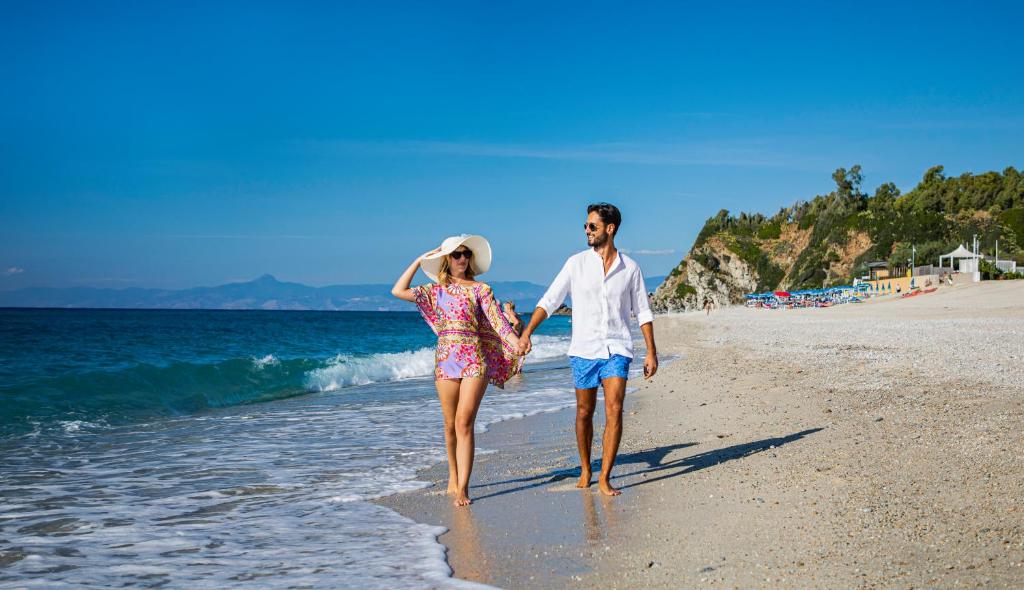 Ein Mann und eine Frau, die am Strand spazieren in der Unterkunft Park Oasi Resort in Zambrone