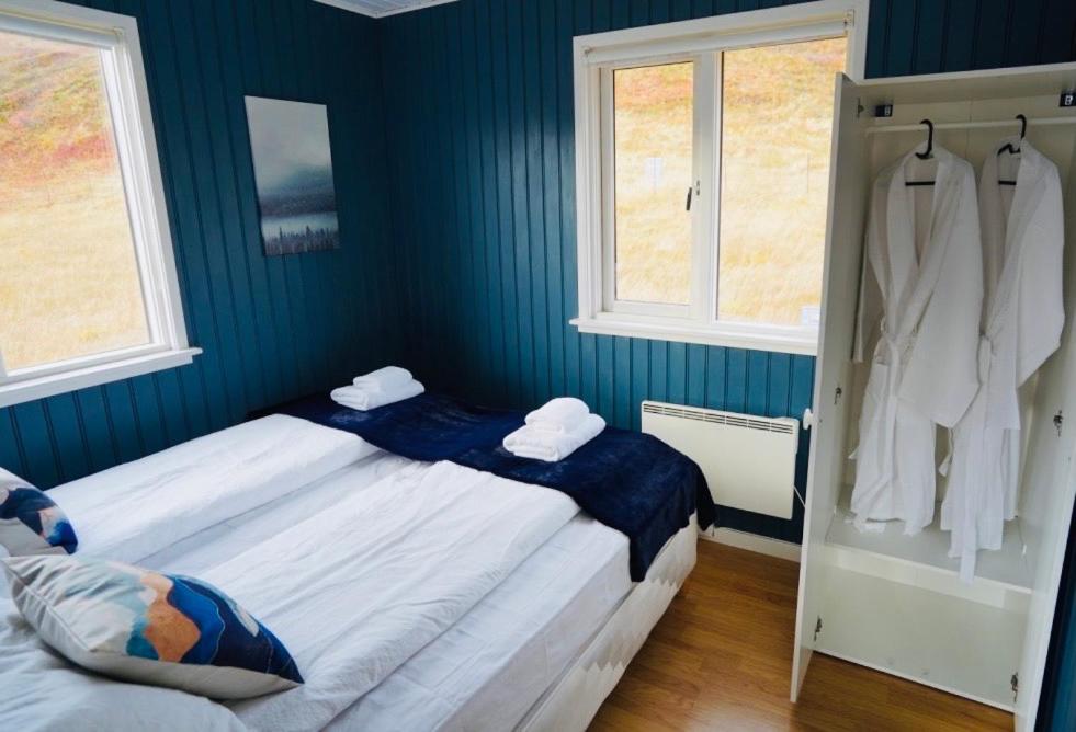 a blue bedroom with two beds and two windows at Langahlid Cottages & Hot Tubs in Seyðisfjörður