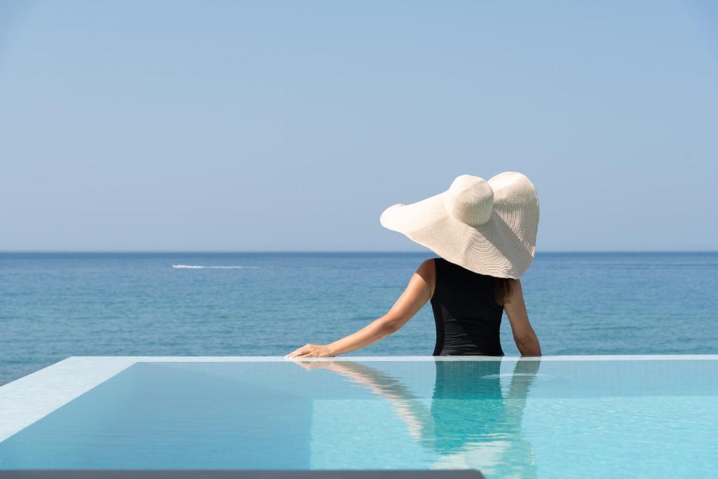 a woman wearing a hat sitting on the edge of a pool at Zen Luxury Villas & Suites, By ThinkVilla in Hersonissos