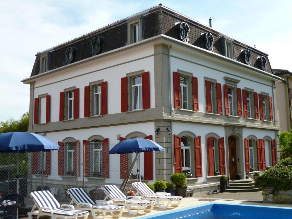 a building with chairs and umbrellas next to a pool at Hôtel Garni Villa Carmen in La Neuveville