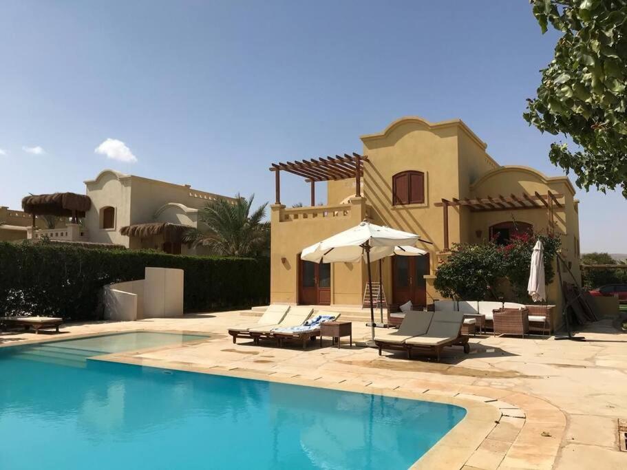 dom z basenem z krzesłami i parasolem w obiekcie Gorgeous Villa in Gouna with Heated Private Pool w mieście Hurghada